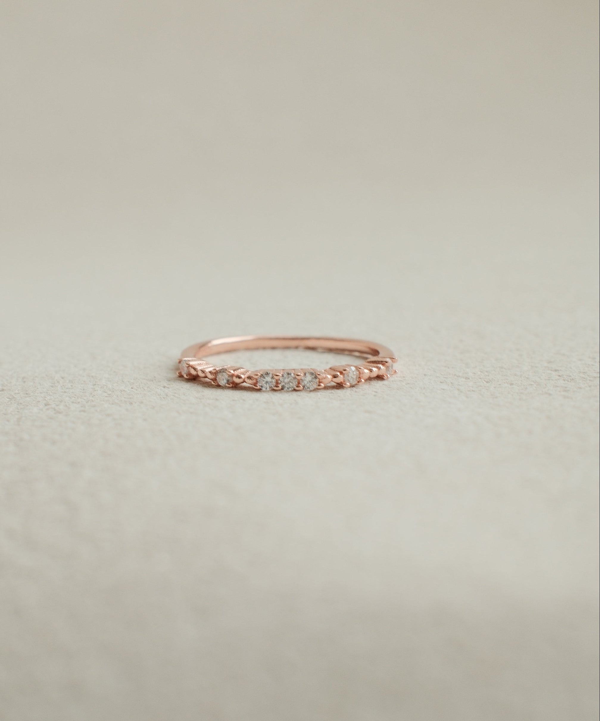 Rose gold ring with small diamonds on a light beige background