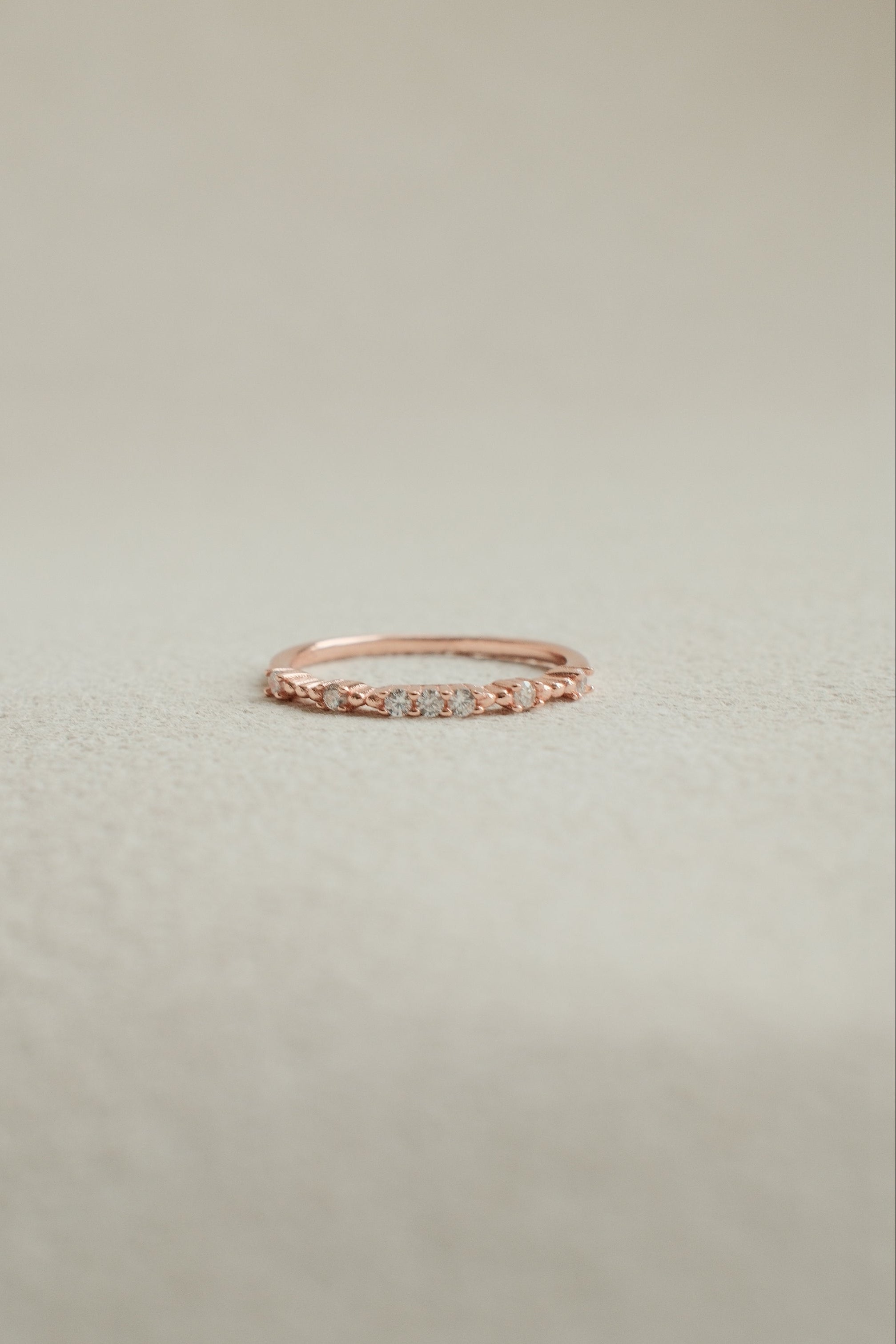 Rose gold ring with small diamonds on a light beige background
