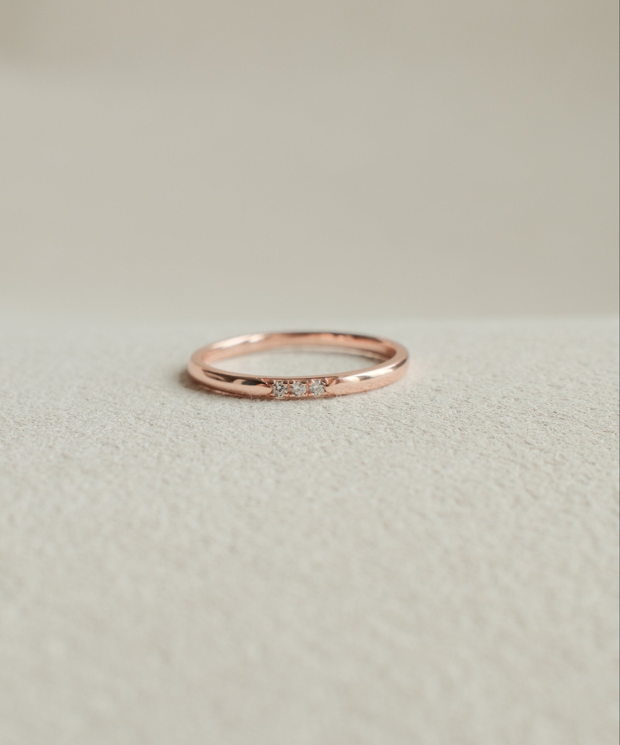 Rose gold ring with small diamonds on a light beige background
