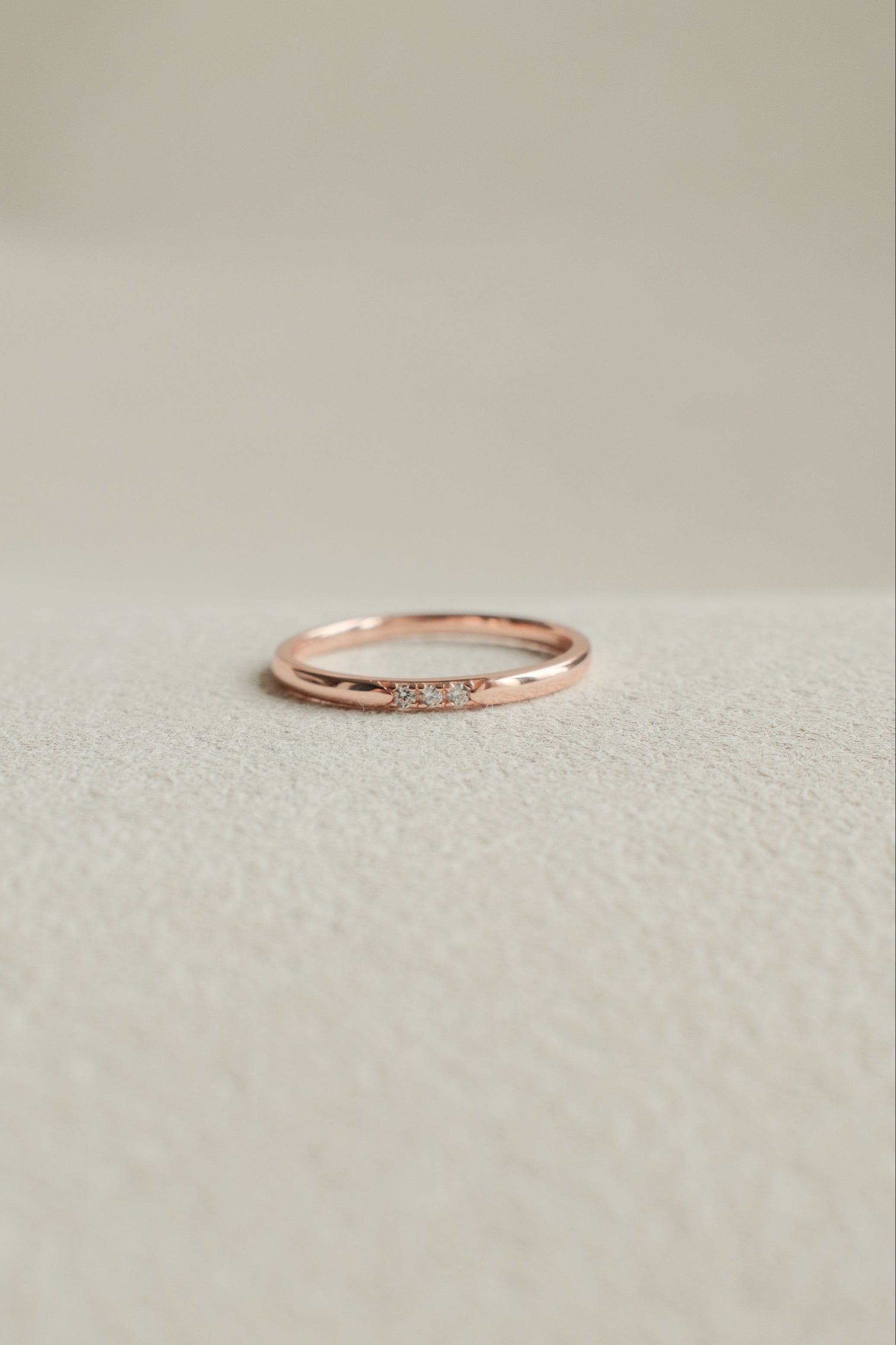Rose gold ring with small diamonds on a light beige background